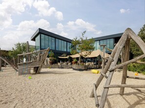 A modern building with large windows, outdoor seating, and a wooden play structure. - Comfortable lodge with dishwasher, in Bloemendaal (Bloemendaal)