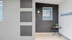 A modern building entrance with a dark facade, a small table with a plant, and a sign reading 'This is our happy place.' - Majestic City Home | Country Club 2 Bedroom Unit (San Juan)