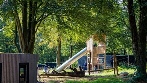 A playground with a slide and climbing structures, surrounded by trees.