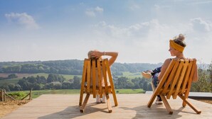 Two people sitting on wooden chairs facing a scenic landscape.