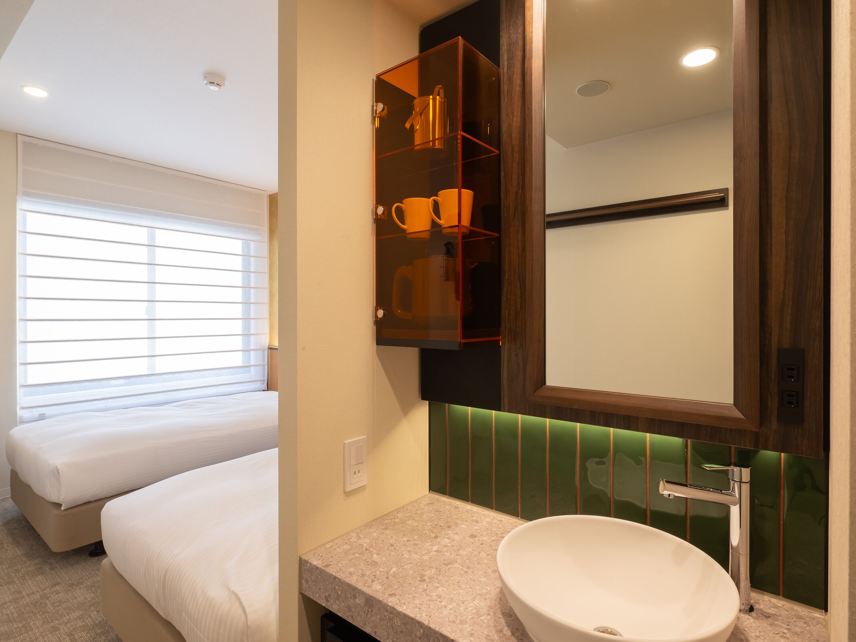 A hotel room with two beds, a bathroom with a large mirror, green-tiled wall, and a white sink.