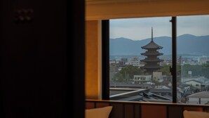 Vista de una pagoda japonesa tradicional a través de una ventana, con un paisaje urbano y montañas al fondo.