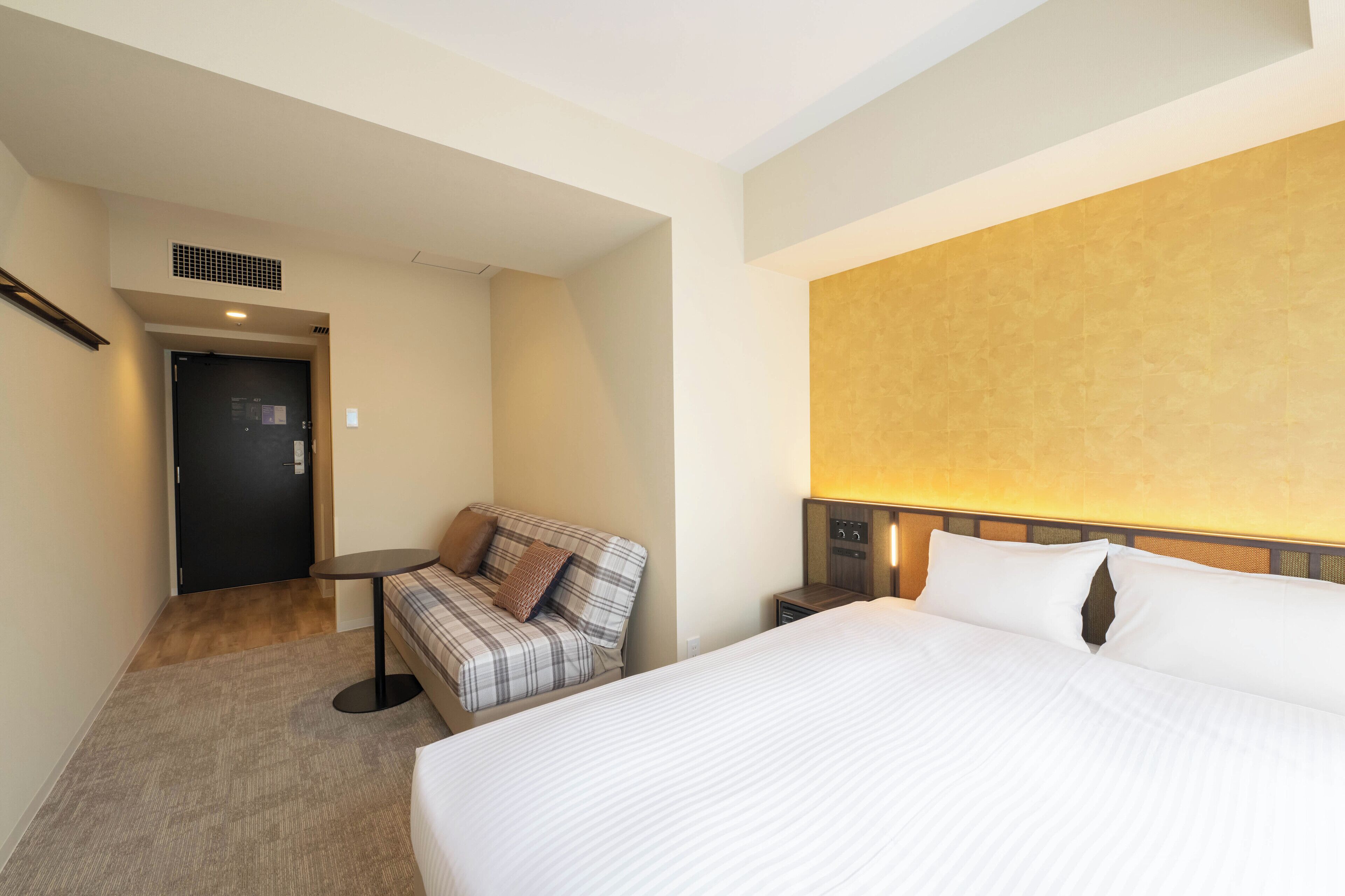 A hotel room with a bed, a sofa, a small table, and a door.