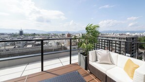 Un balcón con un sofá blanco, una planta en maceta y vistas a un paisaje urbano que incluye una pagoda.