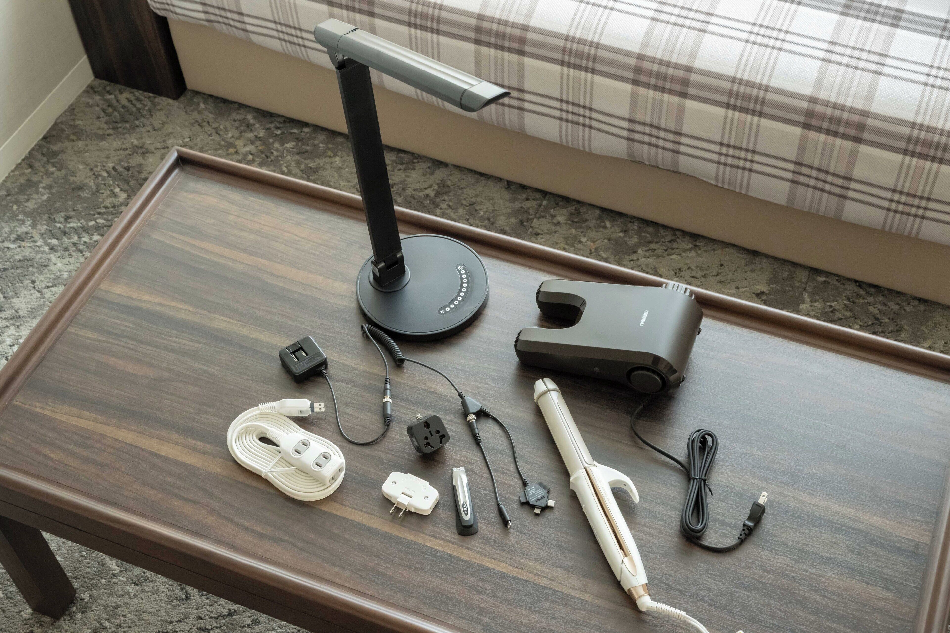 Een houten tafel met een bureaulamp, een haardroger en diverse elektronische accessoires.