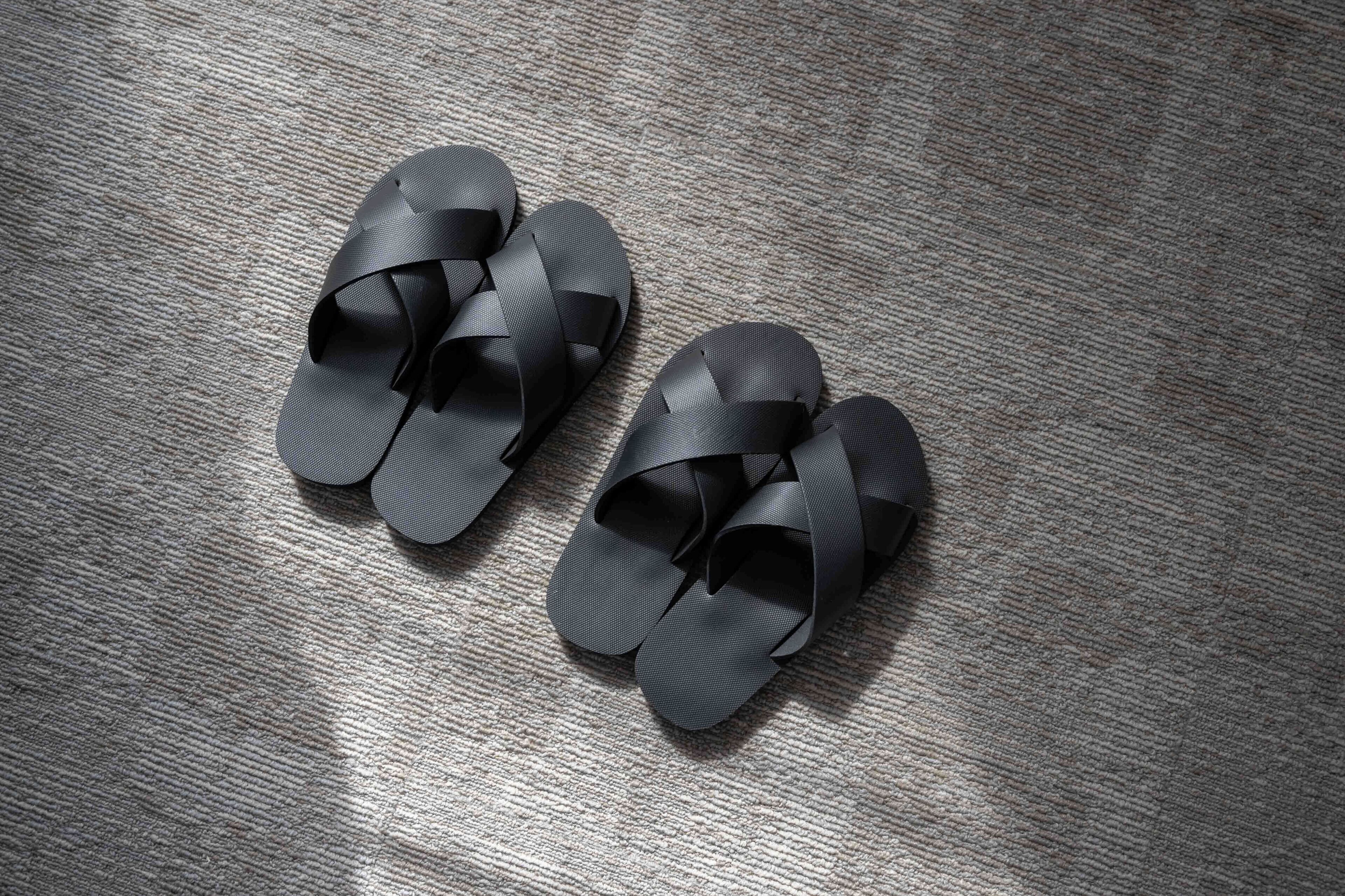 Un par de sandalias negras con diseño tejido sobre un suelo texturizado.