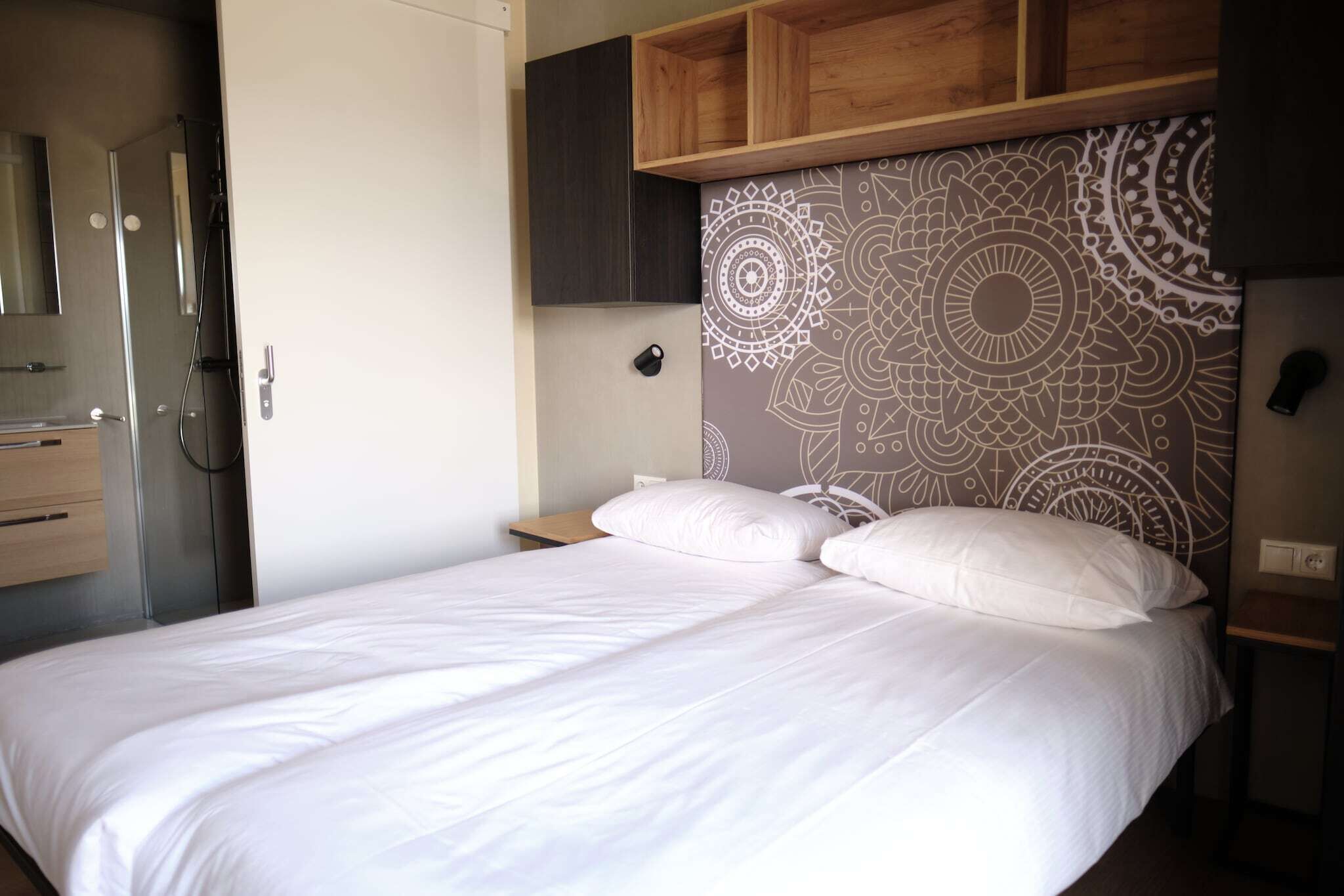 A modern hotel room with a bed, wooden headboard, and built-in wardrobe.