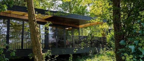 Una cabaña de madera moderna con cerramiento de vidrio, rodeada de un bosque denso.