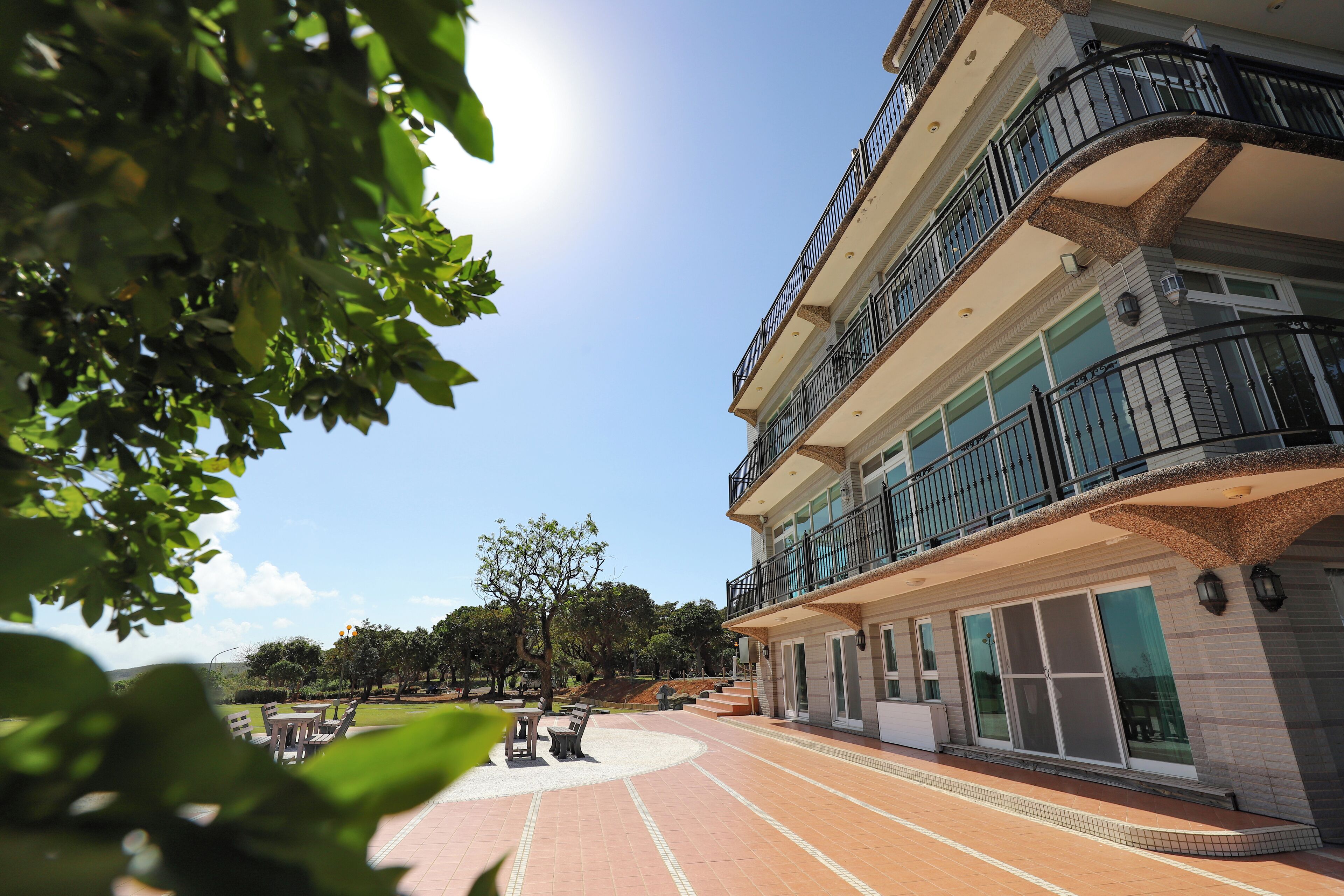 A multi-story hotel with a balcony, outdoor seating area, and a paved courtyard.
