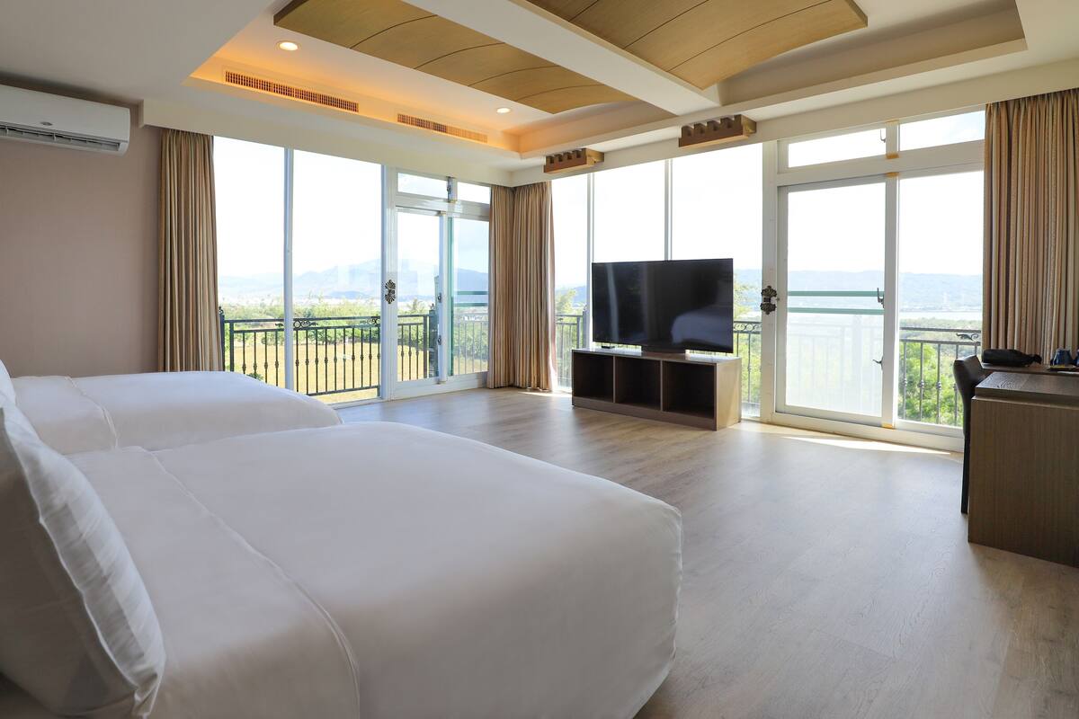 A hotel room with two beds, a TV, and a balcony with a view.