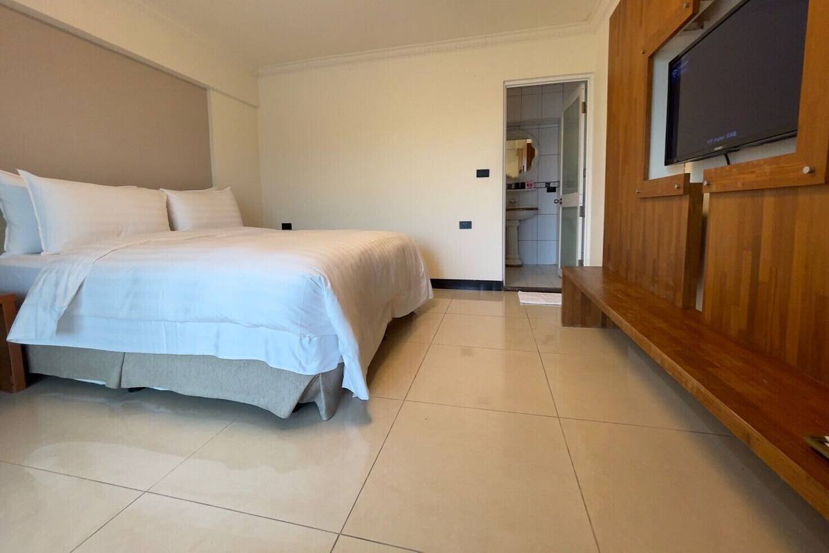 A bedroom with a bed, a wooden TV stand, and a bathroom visible through an open door.