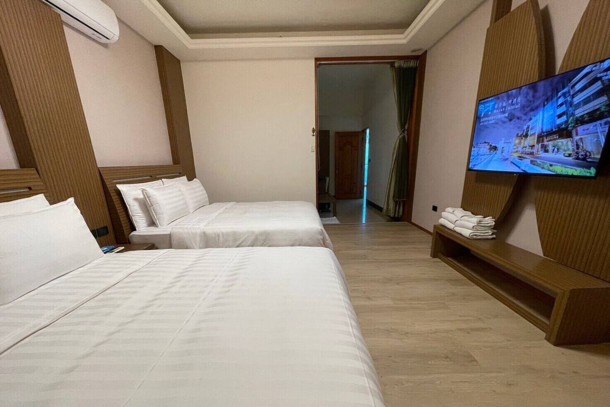 A hotel room with two beds, a TV on the wall, and a wooden bench with towels.
