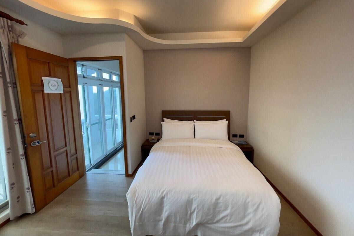 A hotel room with a large bed, a wooden door with a sign, a nightstand, and a window with curtains.