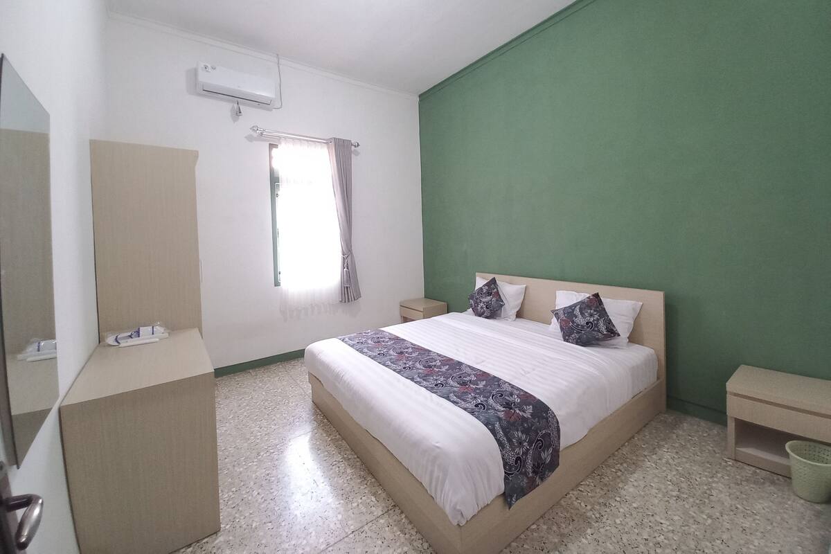 A bedroom with a bed, a nightstand, a dresser, a mirror, a window with curtains, and a green accent wall.