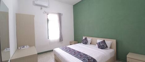 A bedroom with a bed, a nightstand, a dresser, a mirror, a window with curtains, and a green accent wall.