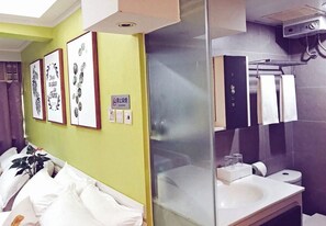A hotel bathroom with a glass partition, a sink, and a mirror. There are towels hanging on a rack and a sign on the wall.
