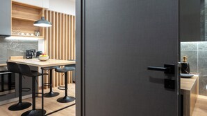 A modern kitchen with a wooden countertop, black bar stools, and a bowl of fruit.