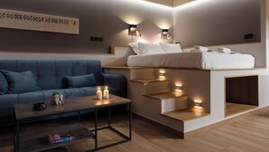 A modern hotel room with a sofa, a coffee table, a bed with built-in steps, and wall-mounted lighting.