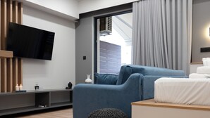 Een moderne woonkamer met een flatscreen televisie, een blauwe bank, een houten tv-meubel en een groot raam met gordijnen.