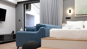 Een moderne slaapkamer met een bed, een blauwe fauteuil, een houten bankje en een televisie aan de muur.