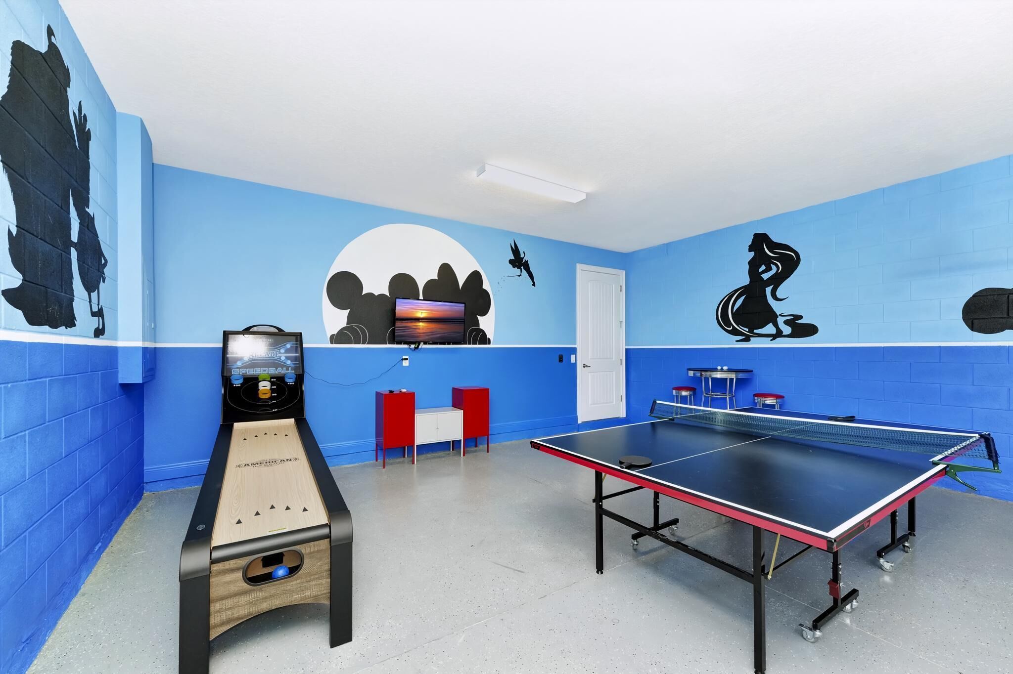 A room with a ping pong table, a foosball table, and a TV.