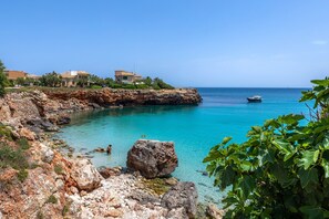 A coastal area with rocky terrain, clear turquoise waters, and a boat in the distance.