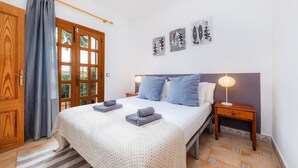 A bedroom with a bed, two bedside tables, a nightstand, a window with curtains, and wall art. - Holiday Home 'Sa Fonteta Cala Morlanda' with Private Terrace, Wi-Fi and Air Conditioning (S'Illot-Cala Morlanda)
