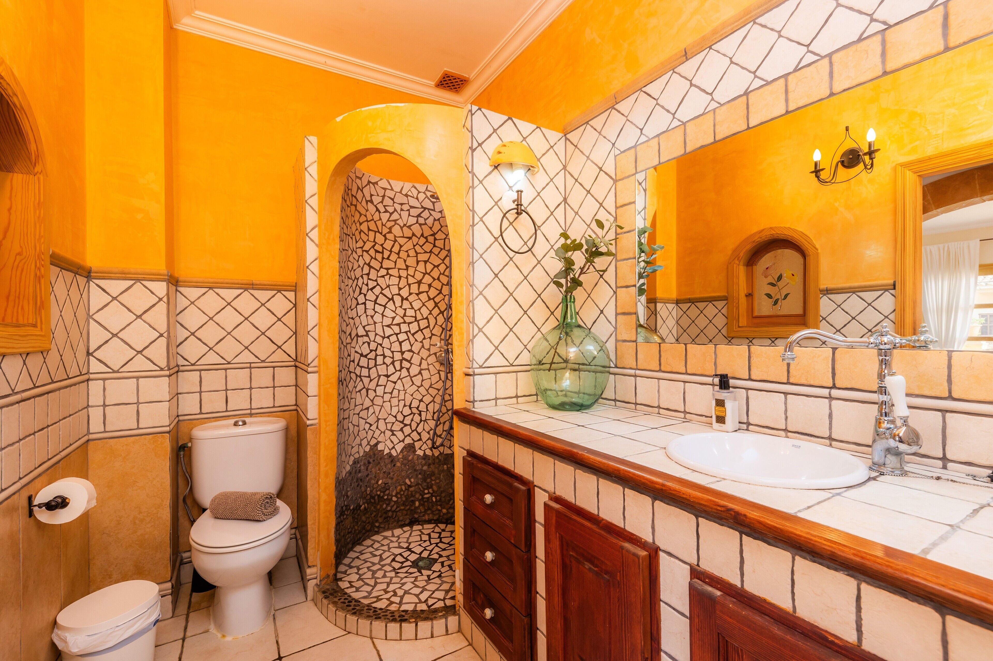 Een badkamer met een mozaïekwand, toilet, wastafel en spiegel.