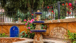 A stone fountain with tiered blue and orange tiles, surrounded by a stone wall and lush greenery. - Holiday Home 'Sa Fonteta Cala Morlanda' with Private Terrace, Wi-Fi and Air Conditioning (S'Illot-Cala Morlanda)