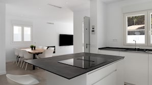 A modern kitchen with a central island, a dining area with white chairs, and a large window. - Villa 'Santa Clara 21a' with Private Pool, Wi-Fi and Air Conditioning (Chiclana de la Frontera)