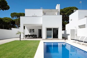 Une maison moderne avec une piscine, un patio doté de chaises et une vue sur les arbres.