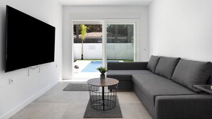 A modern living room with a flat-screen TV, a round coffee table, a grey sofa, and a sliding glass door leading to a pool. - Villa 'Santa Clara 21a' with Private Pool, Wi-Fi and Air Conditioning (Chiclana de la Frontera)