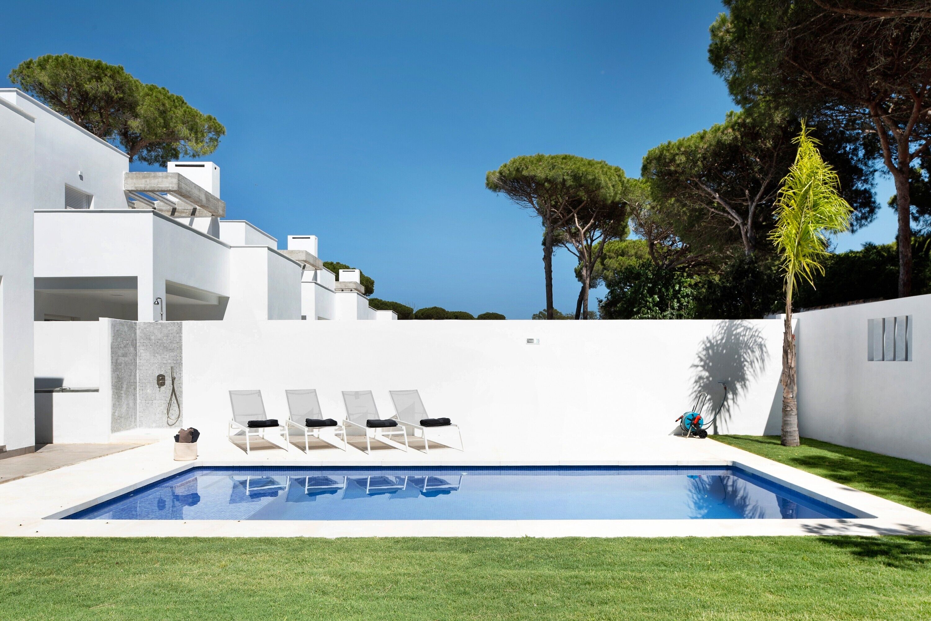 A modern pool area with a clear blue pool, white walls, and a few lounge chairs.