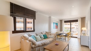 A modern living room with a sofa, a wooden coffee table, a dining area with chairs, and a balcony with a view of the buildings. - Apartment 'Luxury Flat Beach Resort Sea View' with Shared Pool, Wi-Fi and Air Conditioning (Arenales del Sol)