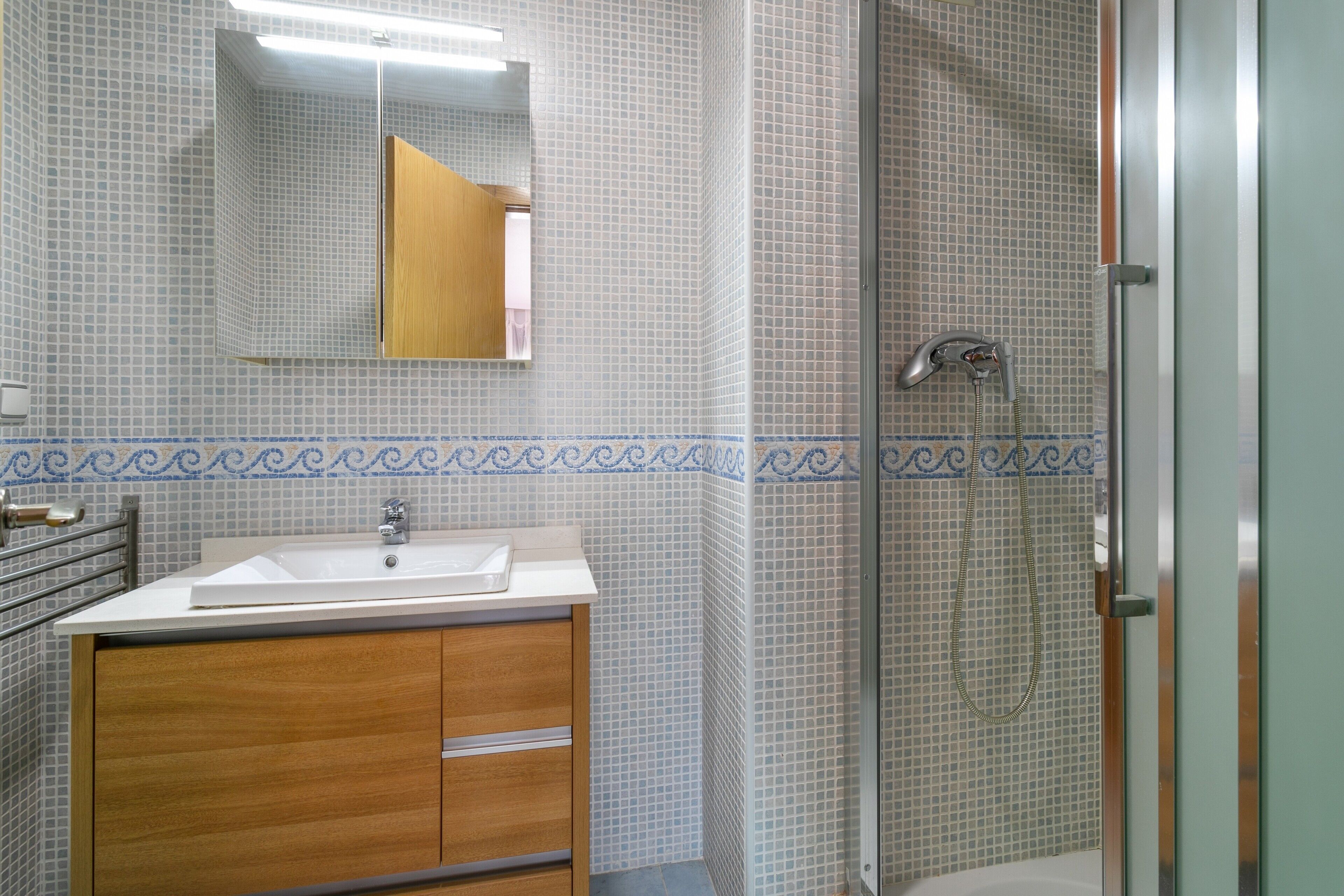 Une salle de bain avec un lavabo, un miroir, une douche et des murs carrelés.