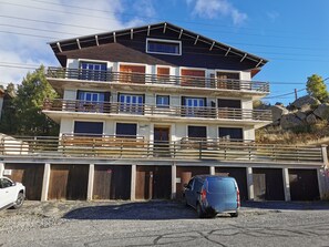 A multi-story building with balconies, a garage, and a parking area.