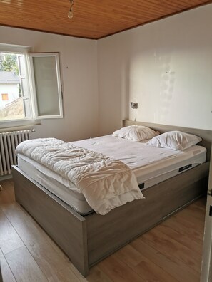 A bedroom with a bed, a window, a radiator, and a wooden ceiling.