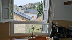 Eine Küche mit integriertem Waschmaschine, einem Fenster mit Blick auf Häuser und einer Kaffeemaschine auf der Arbeitsplatte.