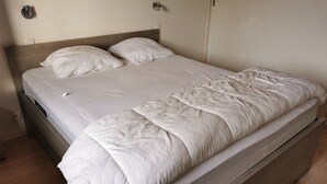 Ein Einzelbett mit hölzernem Kopfteil, weißer Bettwäsche und einer Wandleuchte.