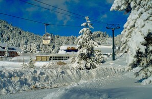 A snow-covered landscape with a ski lift, buildings, and trees.