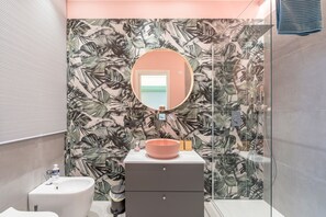 Une salle de bain avec un miroir rond, un lavabo, des toilettes et un espace douche.