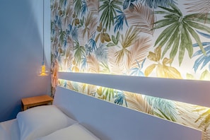 A bedroom with a bed, a nightstand, a wall with a leaf pattern, and a hanging light fixture.