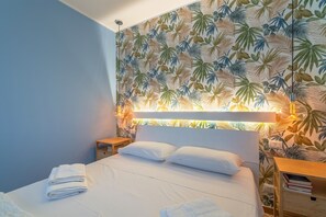Une chambre d’hôtel comprenant un lit, une table de chevet, une commode et un mur orné d’un motif de feuilles.