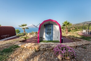 Edifici petit d'una sola planta amb una porta blava, envoltat per una paret de pedra i vistes al mar.