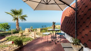 A patio with a table and chairs, a large umbrella, a palm tree, and a view of the sea. - Glamping 'Melograno' with Sea View, Wi-Fi and Air Conditioning (Tusa)