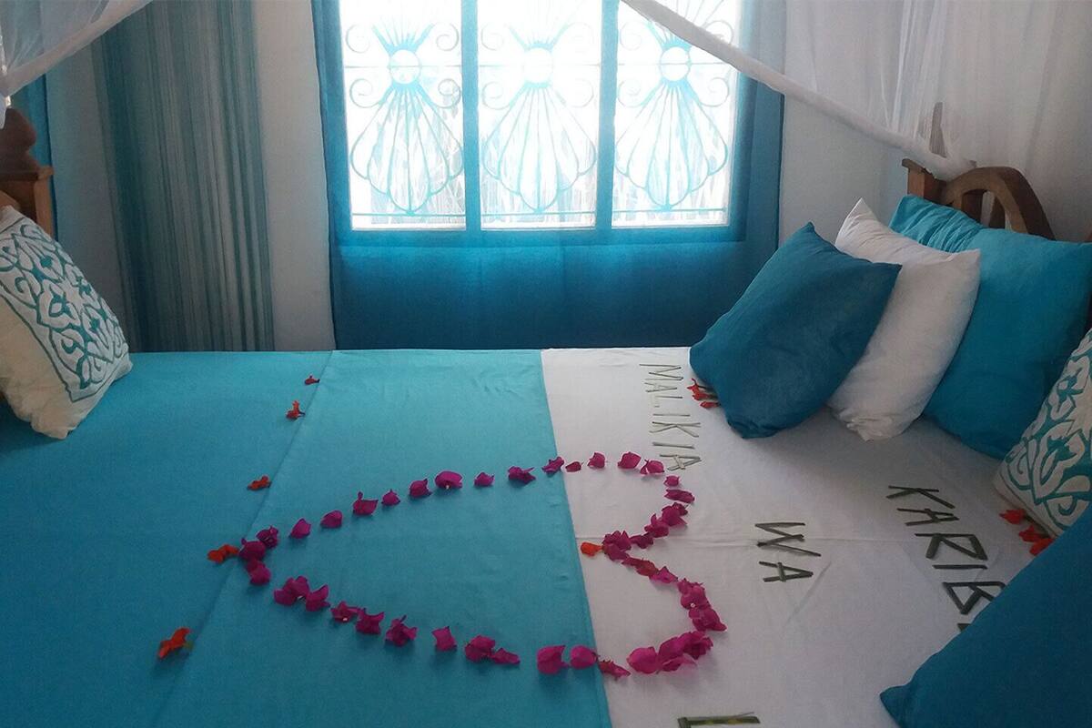 Ein Bett mit blauer Bettdecke, Kissen und einer herzförmigen Girlande aus rosa Blumen.