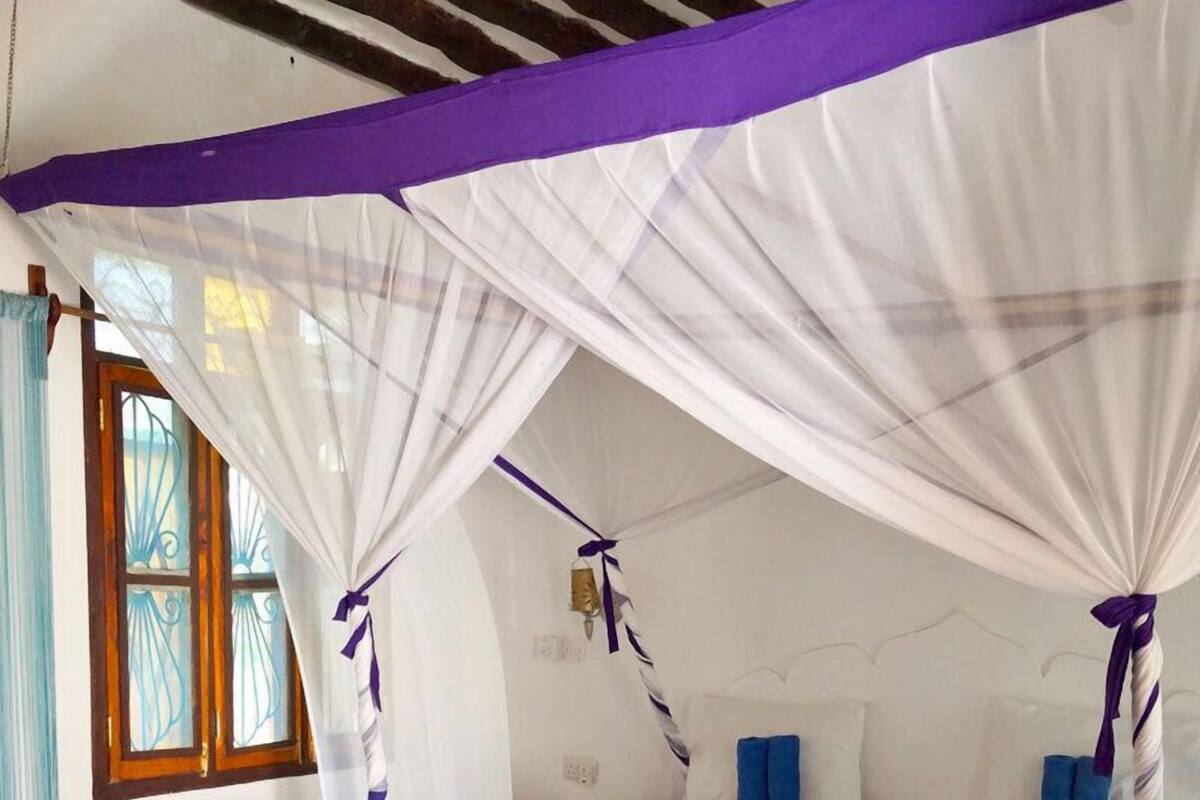 Ein Schlafzimmer mit einem Himmelsbett, einem Fenster mit Vorhängen und einem braunen Boden.