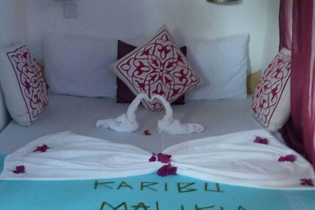 Ein Bett mit Handtuch und Rosenblättern, ein Kissen mit rotem und weißem Muster sowie eine wandmontierte Lampe.