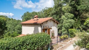 A small, single-story building with a red-tiled roof, surrounded by lush greenery and a dirt path. - Ocabianca Holiday Home with Private Terrace, Wi-Fi and Air Conditioning (Casole d'Elsa)