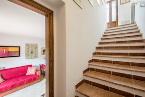 A staircase with wooden steps leading to an upper floor, a red sofa with patterned cushions, and framed botanical prints on the wall.